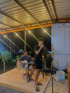 a man standing on a stage with two men playing guitars at Dragonfly Senaru Lodge in Senaru