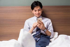 a man sitting in bed looking at his cell phone at Comfort Hotel Kitakami in Kitakami