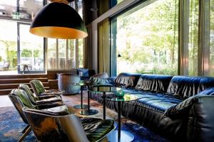 a living room with a couch and tables and a large window at Motel One München - Deutsches Museum in Munich