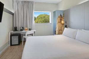 1 dormitorio con cama blanca, escritorio y ventana en B&B HOTEL Barcelona Granollers, en Les Franqueses del Vallès