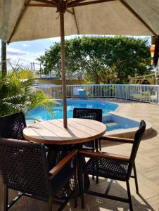 una mesa y sillas bajo una sombrilla junto a una piscina en Casa Villa Real Pousada, en Cabo Frío