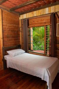 Cama en habitación de madera con ventana en Cabaña Ave Del Paraiso, en Cartago