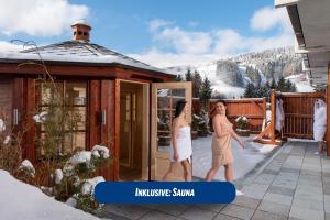 duas mulheres a andar em frente a uma casa na neve em Best Western Ahorn Hotel Oberwiesenthal – Adults Only em Kurort Oberwiesenthal