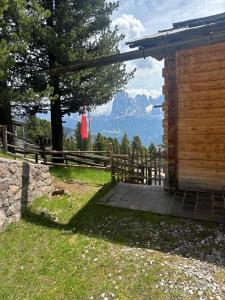 eine Holzhütte mit einem Zaun und Bergen im Hintergrund in der Unterkunft Chalet da mont Resciesa in St. Ulrich in Gröden