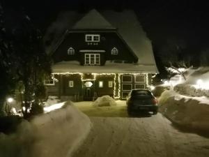 uma casa com um carro estacionado na neve à noite em Prawdzicówka em Zachełmie