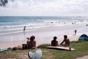 Wategos Beach Shack في خليج بايرون: مجموعة من الناس يجلسون على الشاطئ مع ألواح ركوب الأمواج