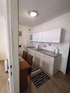 cocina con armarios blancos, fregadero y mesa en Ema Apartmani, en Vinkovci