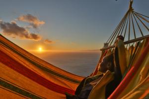 een man in een hangmat die de zonsondergang ziet bij Villa Leonor Cliffside Retreat in Calheta