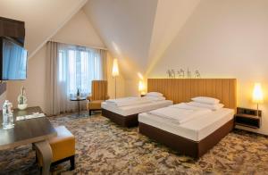 a hotel room with two beds and a desk at ARCOTEL Camino Stuttgart in Stuttgart