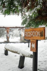 um banco de parque coberto de neve com uma placa em Melewe em Villa La Angostura