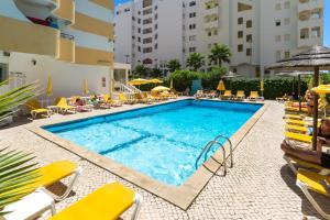 uma piscina com cadeiras amarelas e um hotel em Hotel Atismar em Quarteira