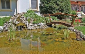 einen Teich mit einer Brücke im Garten in der Unterkunft Hotel Prezident in Palić