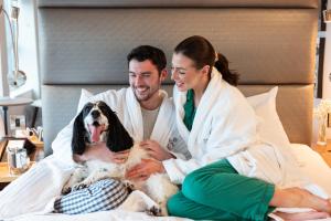 Un uomo e una donna seduti su un letto con un cane di Sandman Signature Newcastle Hotel a Newcastle upon Tyne