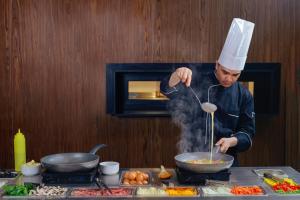 un hombre en un chef sombrero cocinando comida en un wok en Byblos Hotel, en Abiyán