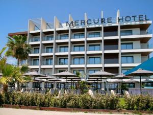 un hôtel avec des chaises et des parasols devant lui dans l'établissement Mercure Larnaca Beach Resort, à Larnaka