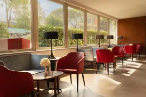 a waiting room with red chairs and tables and windows at Hotel American Palace Eur in Rome