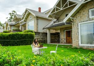 een vrouw in een stoel voor een huis met een laptop bij AJ Gable Clouds Ooty by VOYE HOMES - Serene Stay Near Avalanche Emerald Lake in Ooty