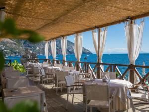 un restaurant avec des tables et des chaises blanches et l'océan dans l'établissement Hotel Le Agavi, à Positano