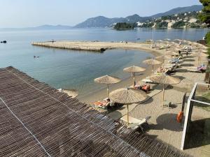 - une plage avec des parasols et des personnes assises sur le sable dans l'établissement Corfu Holiday Palace, à Corfou