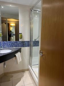 ein Bad mit einer Dusche, einem Waschbecken und einer Tür in der Unterkunft Holiday Inn Express London - Epsom Downs, an IHG Hotel in Epsom