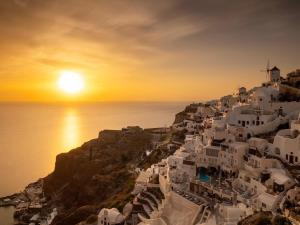 un groupe de bâtiments blancs sur une colline au coucher du soleil dans l'établissement Art Maisons Oia Castle, à Oia