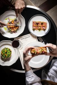 una persona sosteniendo una porción de pizza en una mesa con platos de comida en Hôtel Des Grands Voyageurs, en París