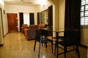 een woonkamer met een glazen tafel en stoelen bij Meridian Rooms and Service Apartment in Mysore