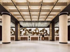 une femme debout dans un hall avec un mur d'art dans l'établissement Fairmont The Queen Elizabeth, à Montréal