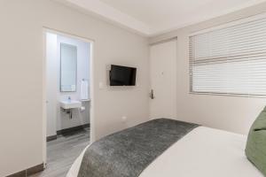 a white bedroom with a bed and a television at STAY Menlyn in Pretoria