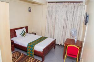 um quarto com uma cama, uma mesa e uma janela em Kenendia Hotel em Kampala