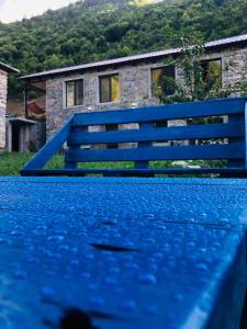 a blue bench in the rain with a house in the background at River side SVANETI in Mestia