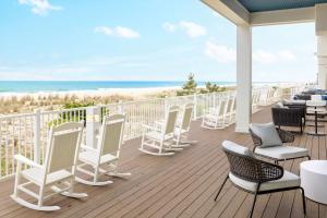 um deque com cadeiras e mesas brancas e a praia em Hilton Garden Inn Ocean City Oceanfront em Ocean City