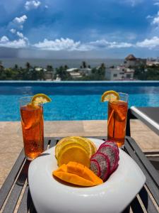 a plate of fruit on a table with two drinks at Areia Boutique Hotel - Puerto Morelos in Puerto Morelos