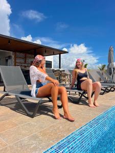 two women sitting on chairs next to a swimming pool at Areia Boutique Hotel - Puerto Morelos in Puerto Morelos