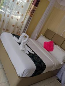 een bed met een roze kussen en handdoeken erop bij ODELIA GARDENS HOTEL-Kisumu CITY in Kibos