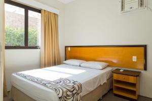 Schlafzimmer mit einem Bett mit einem Kopfteil aus Holz und einem Fenster in der Unterkunft Golden Suíte Hotel in Campinas