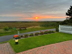 einen Sonnenuntergang über einem Garten mit einer Bank und Blumen in der Unterkunft Haus Amanda in Norddorf