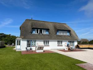 ein Haus mit einem Strohdach und Stühlen im Hof in der Unterkunft Haus Amanda in Norddorf