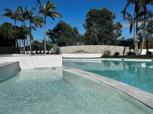 a swimming pool with blue water and palm trees at Atlantis Marcoola in Marcoola