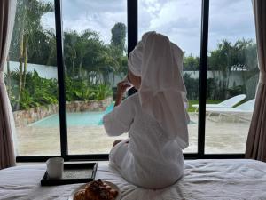 a woman sitting on a bed looking out a window at Tropical Pool Villa near Fishermans Village in Bophut 