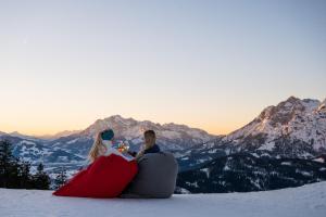 um homem e uma mulher sentados no topo de uma montanha coberta de neve em Aparthotel Bergtraum em Mühlbach am Hochkönig