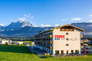 a building with a google sign on it with mountains in the background w obiekcie COOEE alpin Hotel Kitzbüheler Alpen w mieście Sankt Johann in Tirol