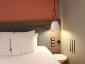 ein Schlafzimmer mit einem Bett mit weißen Kissen und einer Lampe in der Unterkunft Novotel Suites Rouen Normandie in Rouen