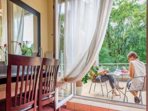 una donna seduta a un tavolo su un balcone che guarda fuori dalla finestra di Hotel Liburnia a Cieszyn