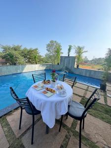 - une table avec une nappe et des chaises blanches à côté de la piscine dans l'établissement OCEAN CREST LUXURY VILLA Mahabaleshwar, à Mahabaleshwar