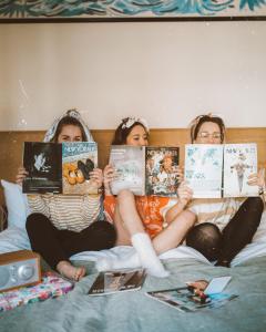 three girls sitting on a bed reading books at Freehand New York in New York