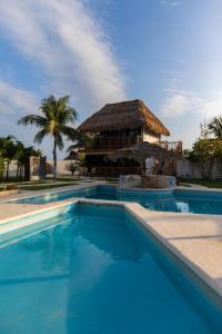 a swimming pool with a thatched building in the background at Kabañas Ojo de Agua in Puerto Morelos