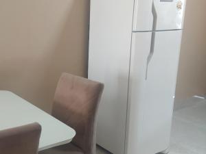 a white refrigerator next to a table and a chair at Casa de 2 quartos com ar, banheiros, pátio, mobília, tudo privativo - Projeto Suítes que Desconta duração e entra 15h adiante inclusive à noite in Sorriso