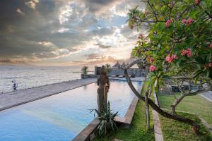 kobieta stojąca obok basenu nad oceanem w obiekcie Ganesh Beach Hotel w mieście Candidasa