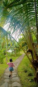 Balé Sebaya - Bungalows Café Nature في سينارو: a little girl walking down a path with a palm tree